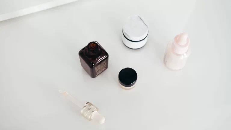 From above of open flacon of aroma oil near pipette and beauty products on smooth white surface