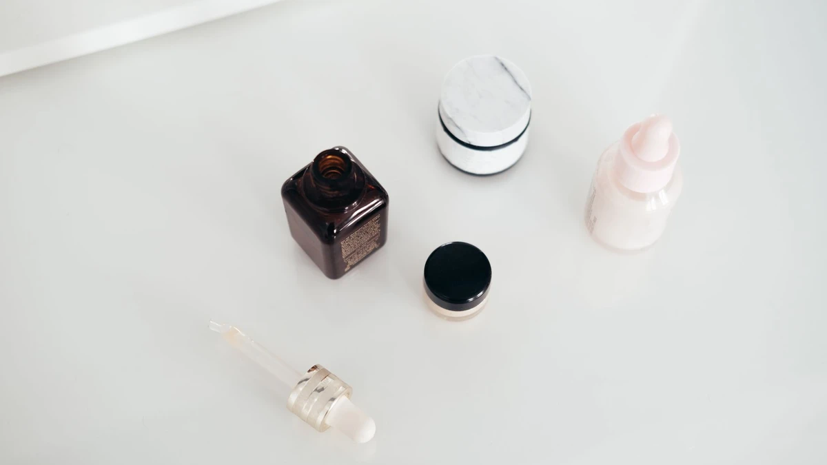 From above of open flacon of aroma oil near pipette and beauty products on smooth white surface