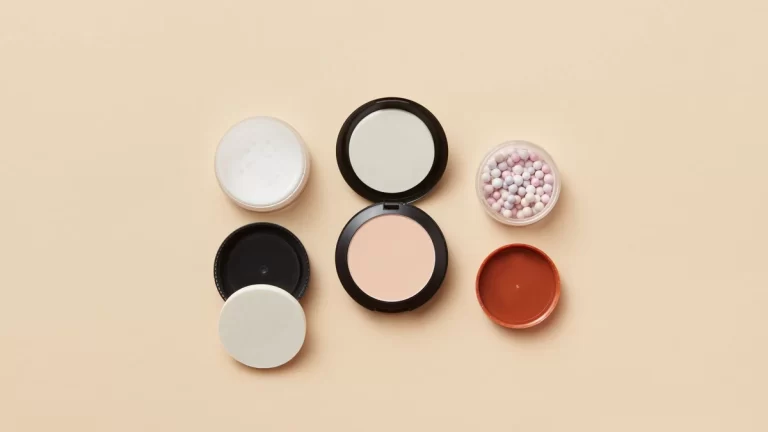 Flat lay of assorted makeup containers and powder balls on a beige surface, showcasing beauty essentials