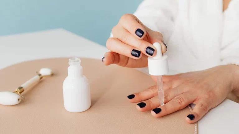 Close-up of a woman applying nail oil with a dropper for manicure care on blue background
