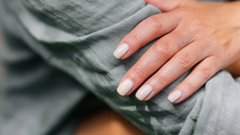 Close-up of a neatly manicured hand resting on a green sleeve, showcasing neutral nail polish