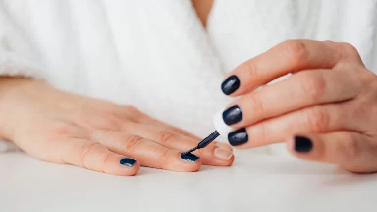 A woman applying dark nail polish at home, showcasing beauty and self-care