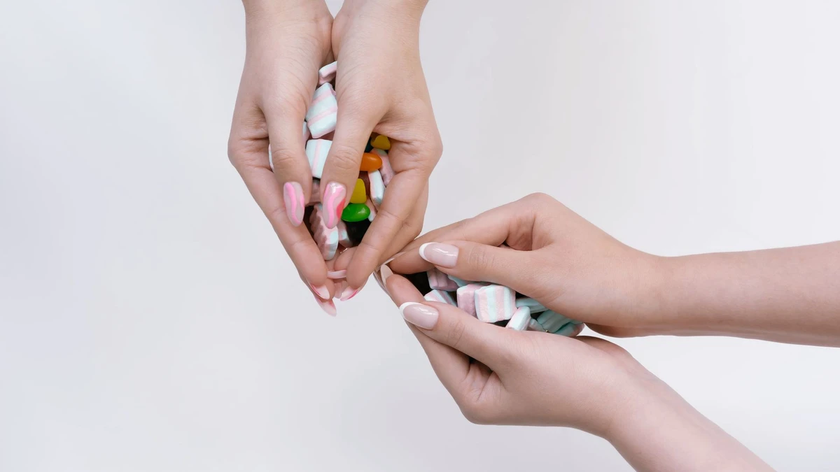 Three hands holding a mix of colorful candies on a white background, showcasing manicured nails