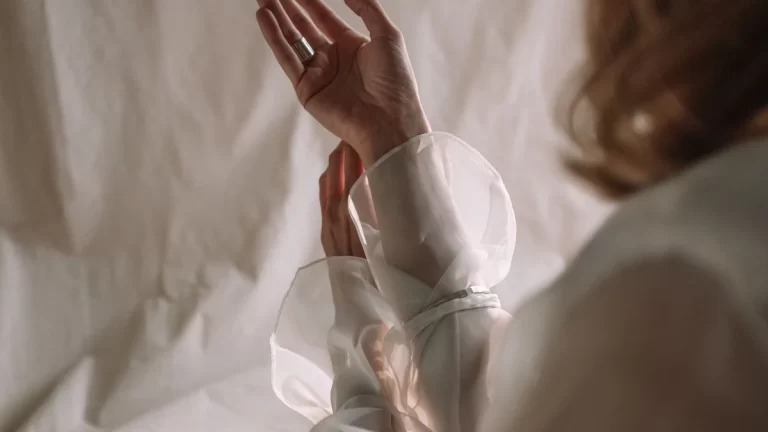 A close-up of hands making a graceful gesture with sheer fabric delicately lit