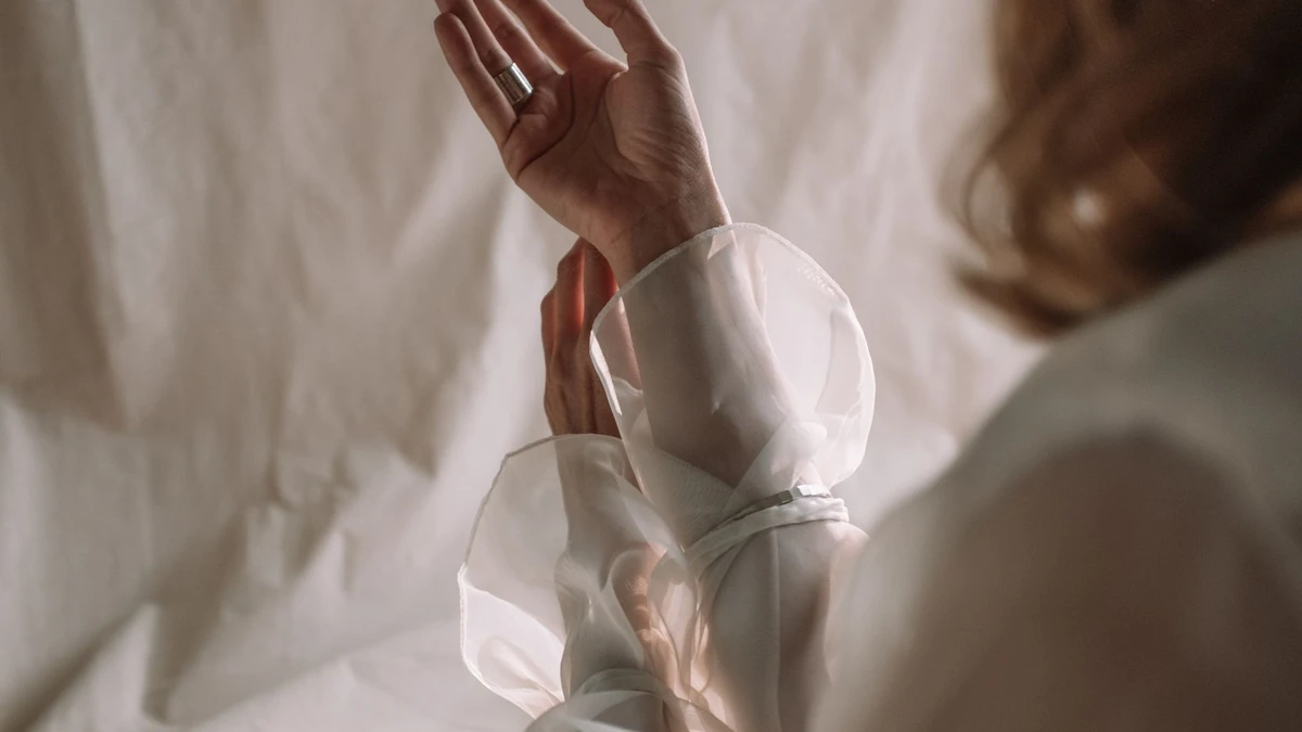 A close-up of hands making a graceful gesture with sheer fabric delicately lit