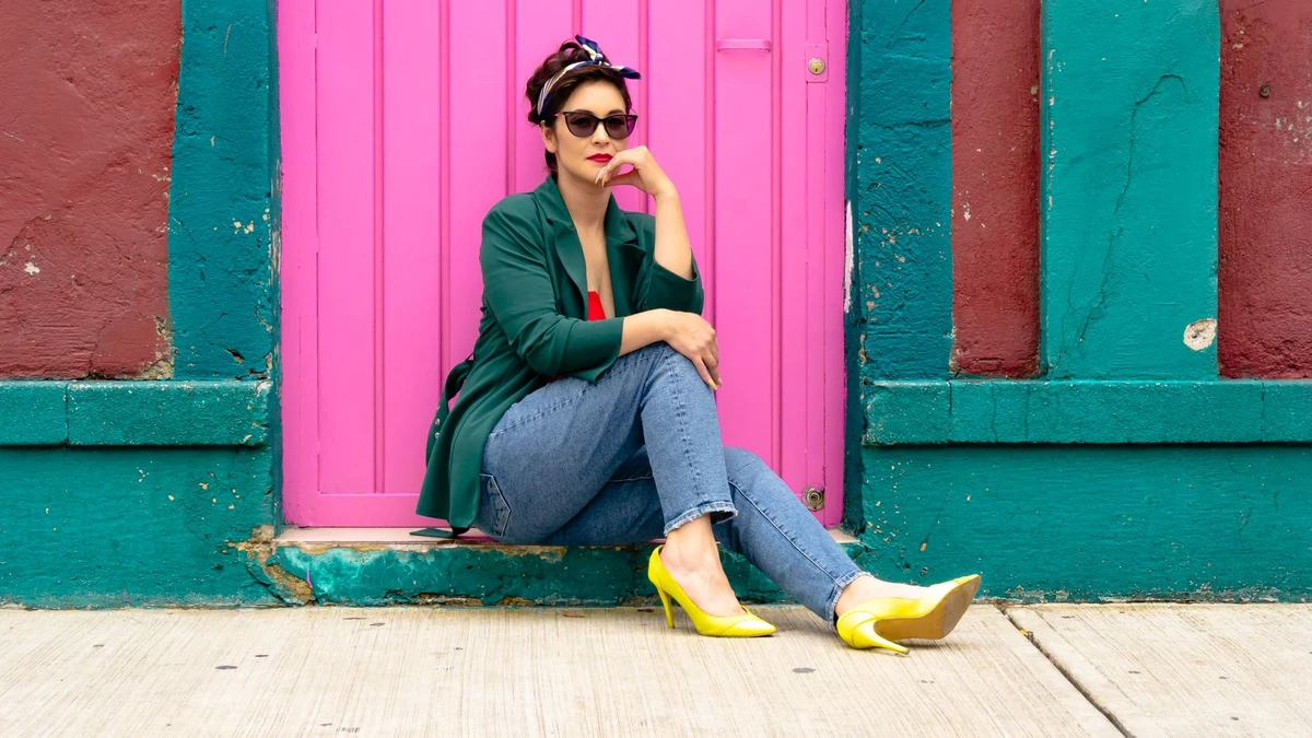 Fashionable woman sitting by a vibrant pink door wearing denim and yellow heels